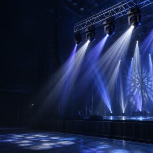 Hybrid moving head lights projecting narrow beams and patterned spot effects on a stage.