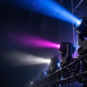 Professional moving head lights mounted on a stage truss and projecting colored beams.