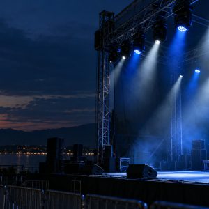 Outdoor concert stage lighting fixtures illuminating a venue at blue hour.